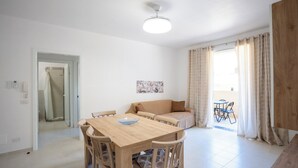 A spacious living area with a wooden dining table, a sofa, and a small balcony with a table and chairs. - Casa Vacanze D&G (Marina di Ragusa)