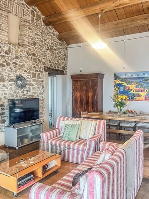 Una sala de estar acogedora con pared de piedra, techo de madera, televisor, sofá a rayas, aparador de madera y un cuadro.