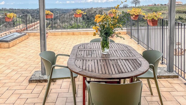 Un porche cubierto con una mesa redonda y sillas, un florero con flores y vistas al campo.