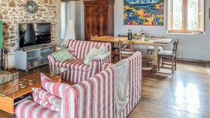 Un espacio de sala acogedor con pared de piedra, un televisor de pantalla plana, sofás a rayas, una mesa de comedor de madera y un mural colorido.