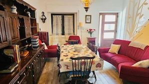 Un salón acogedor con un aparador de madera, un sofá rojo, una mesa de comedor con mantel estampado y una araña.
