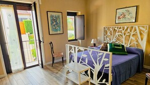 Un dormitorio con cama, una silla, una mesita y una puerta que da a un balcón.