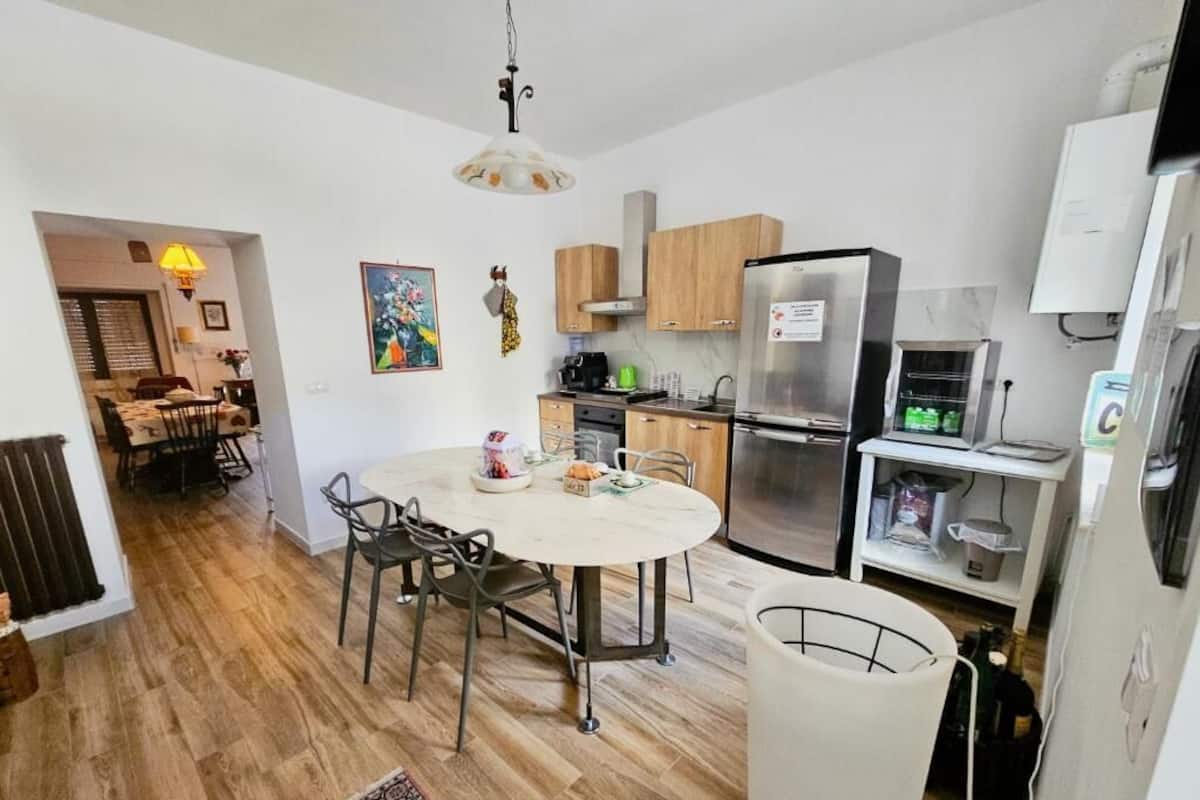 A modern kitchen with a dining area, wooden cabinets, a stainless steel refrigerator, and a white table with chairs.