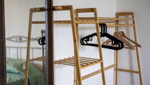 A wooden multi-tiered drying rack with hangers, a bed with a green bedspread, and a mirror reflecting the room. - Il Tasso (Vallerano)