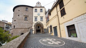 A cobblestone street leading to a historic building with a clock tower and a sign reading "MACELLIO." - Il Tasso (Vallerano)