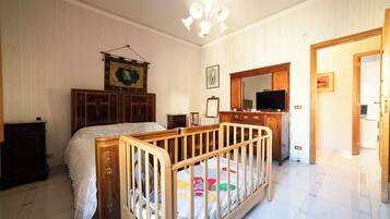 A bedroom with a wooden crib, a dresser, a television, and a mirror.