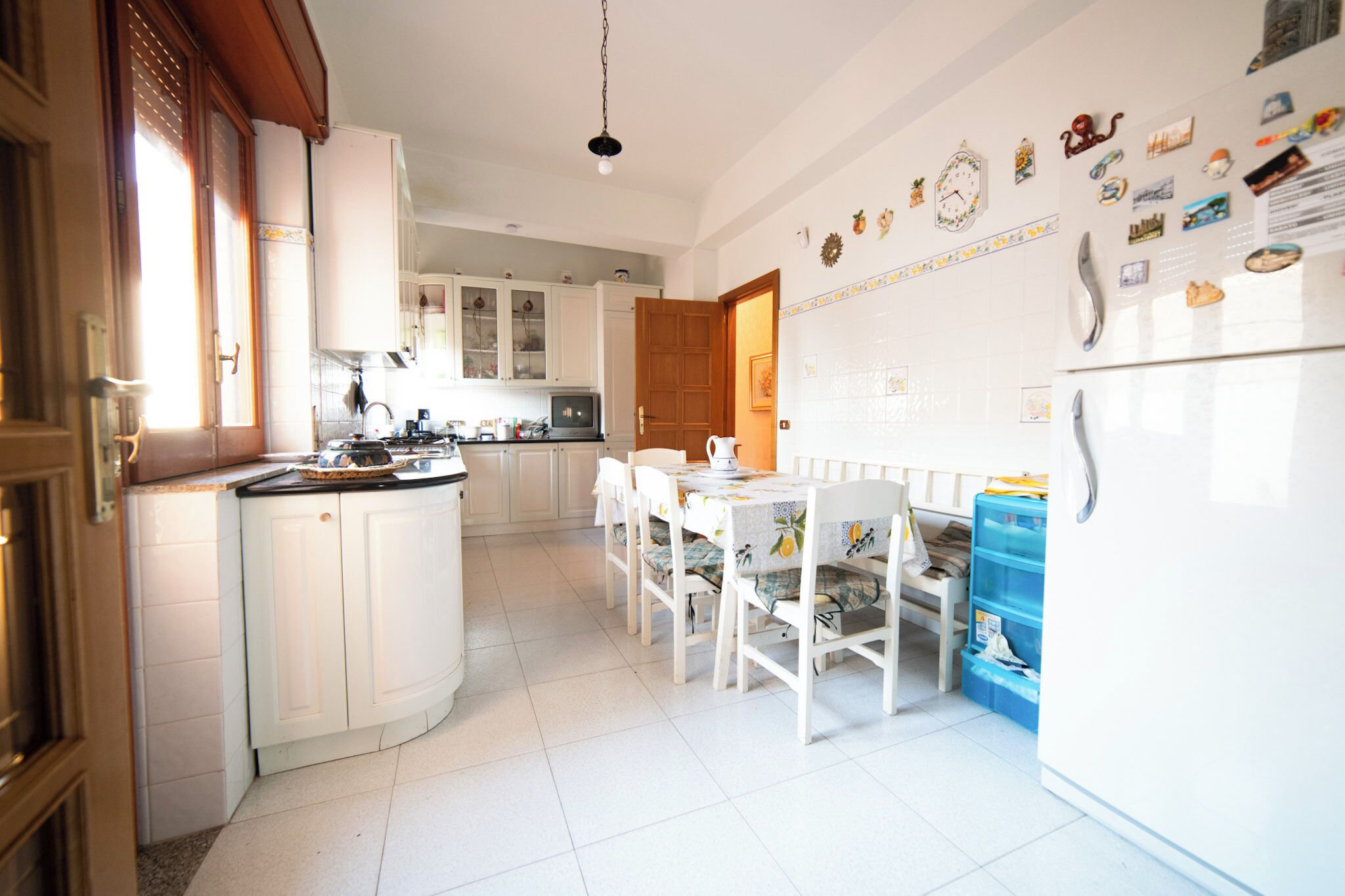 Una cocina con armarios blancos, una mesa de comedor con sillas y un refrigerador.
