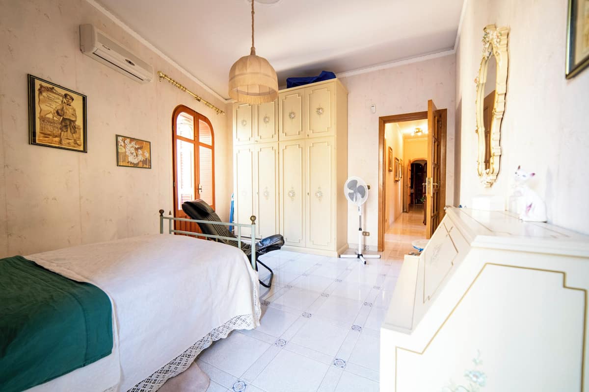 Quarto com duas camas, um guarda-roupa, um espelho e um ventilador.