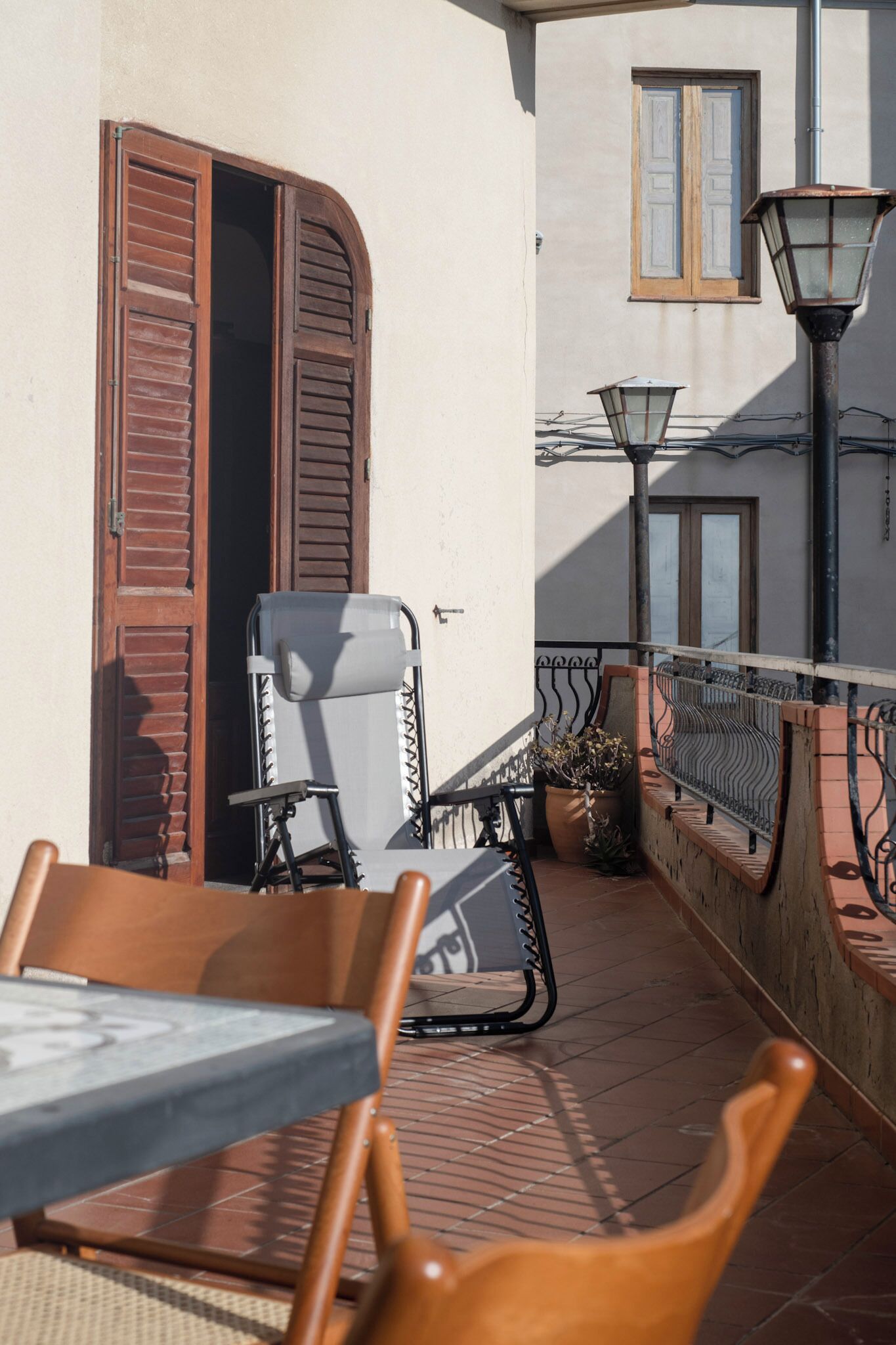 A balcony with a table and chairs, a potted plant, and a lamp post.