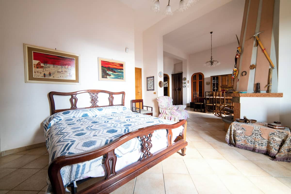 Um quarto espaçoso com uma cama grande, uma cadeira de madeira e uma mesa de jantar com toalha.