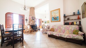 A spacious living room with a wooden dining table, chairs, a floral sofa, and a bookshelf. - Il Rifugio Del Templare (Roccavaldina)