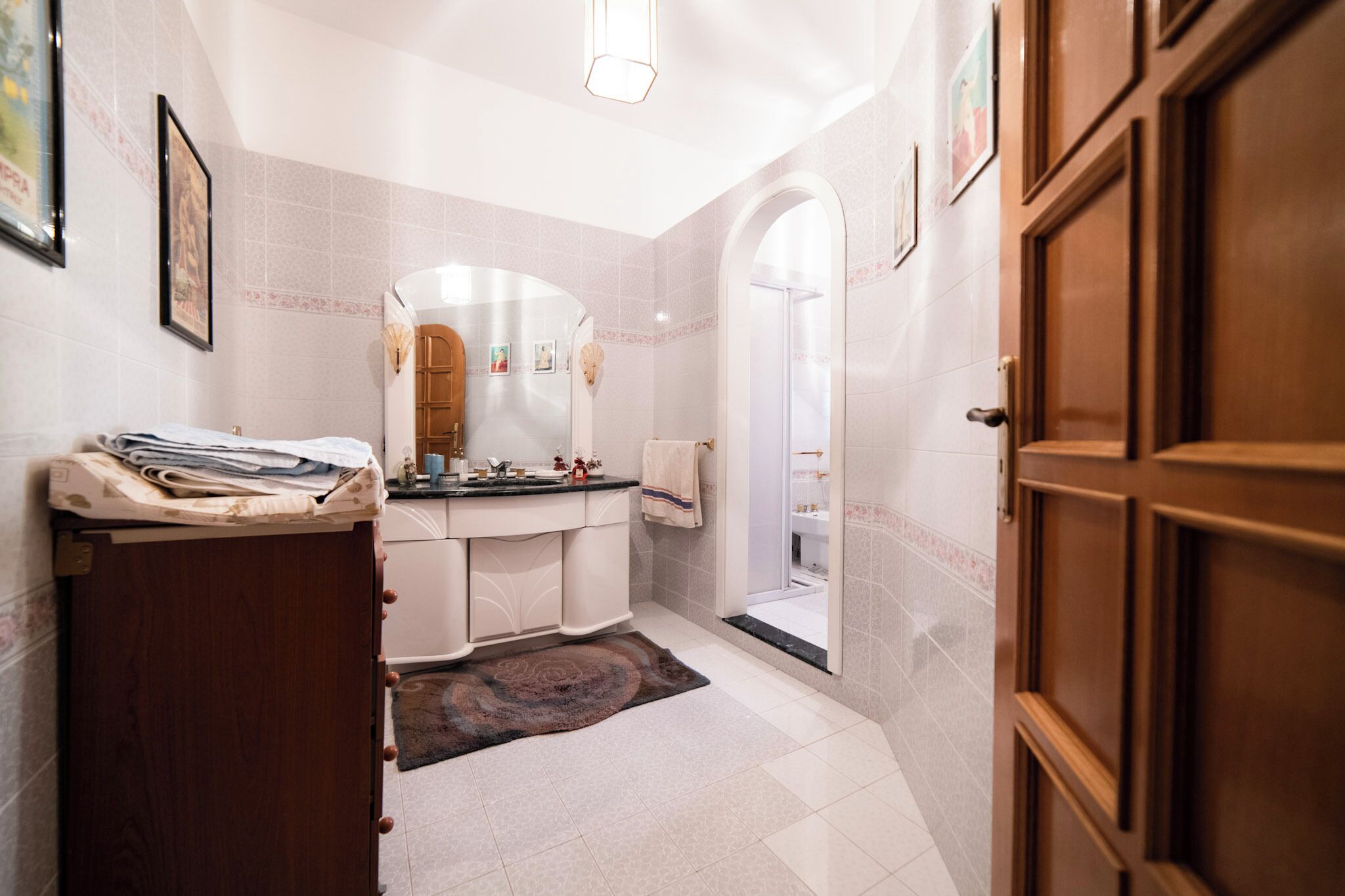 A bathroom with a wooden door, a sink with a mirror, and a shower area.
