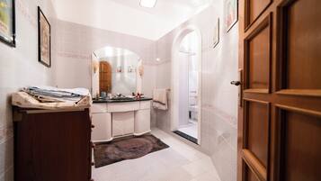 A bathroom with a wooden door, a sink with a mirror, and a shower area.