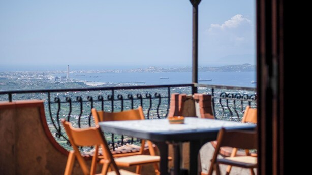 A terrace with a table and chairs, overlooking a cityscape and a body of water. - Il Rifugio Del Templare (Roccavaldina)