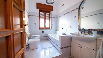 A bathroom with a toilet, bidet, bathtub, and sink.