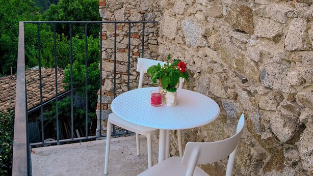 A round white table with two chairs on a balcony with stone walls, overlooking a forested hillside. - B&B Nonna Cristina (Nardodipace)