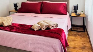 A bed with a red and pink bedspread, two red pillows, and two beige towels. There are two bedside tables with lamps and a small plant. - B&B Nonna Cristina (Nardodipace)
