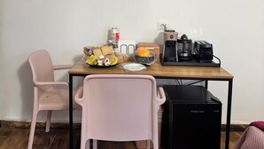 A small kitchenette with a wooden table, two pink chairs, a coffee maker, a blender, and a refrigerator. - B&B Nonna Cristina (Nardodipace)