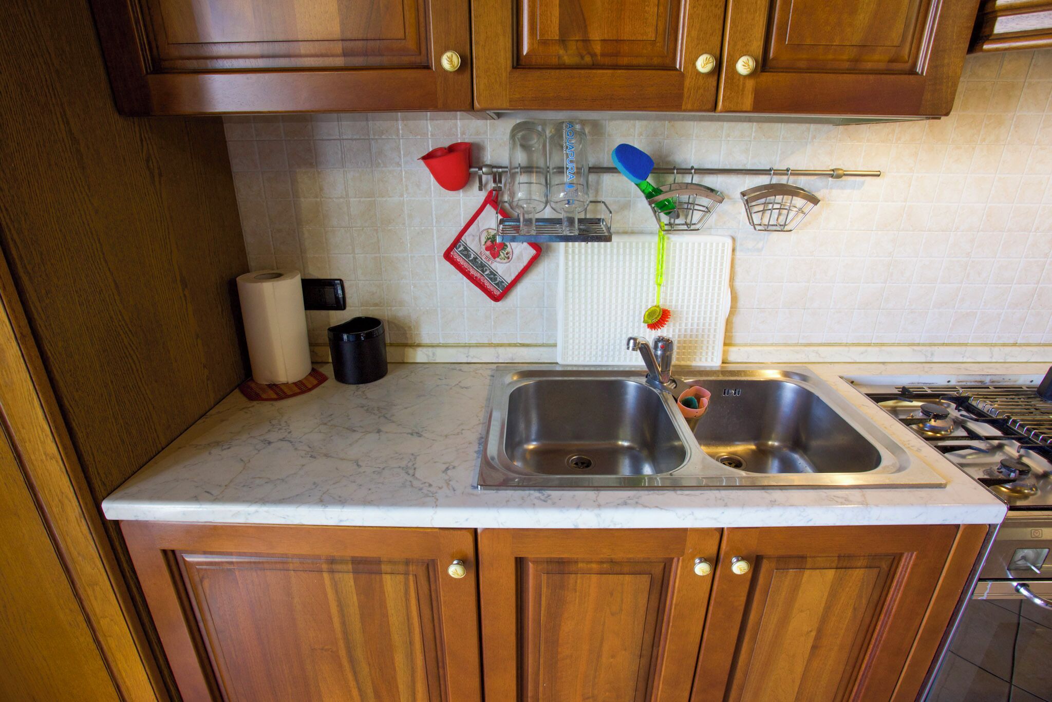 A kitchen with wooden cabinets, a stainless steel sink, and a marble countertop.
