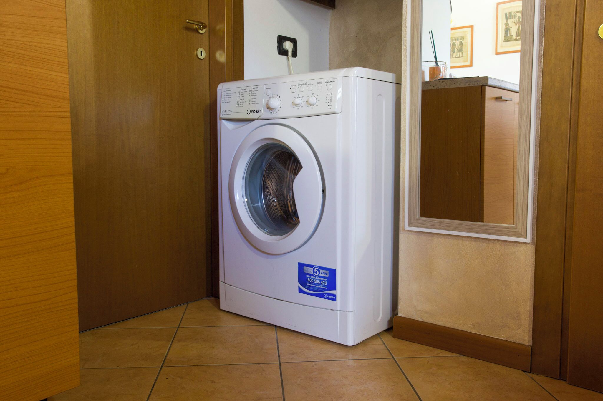 Lavadora de carga frontal en un rincón de una habitación con puertas de madera y suelo de baldosas.