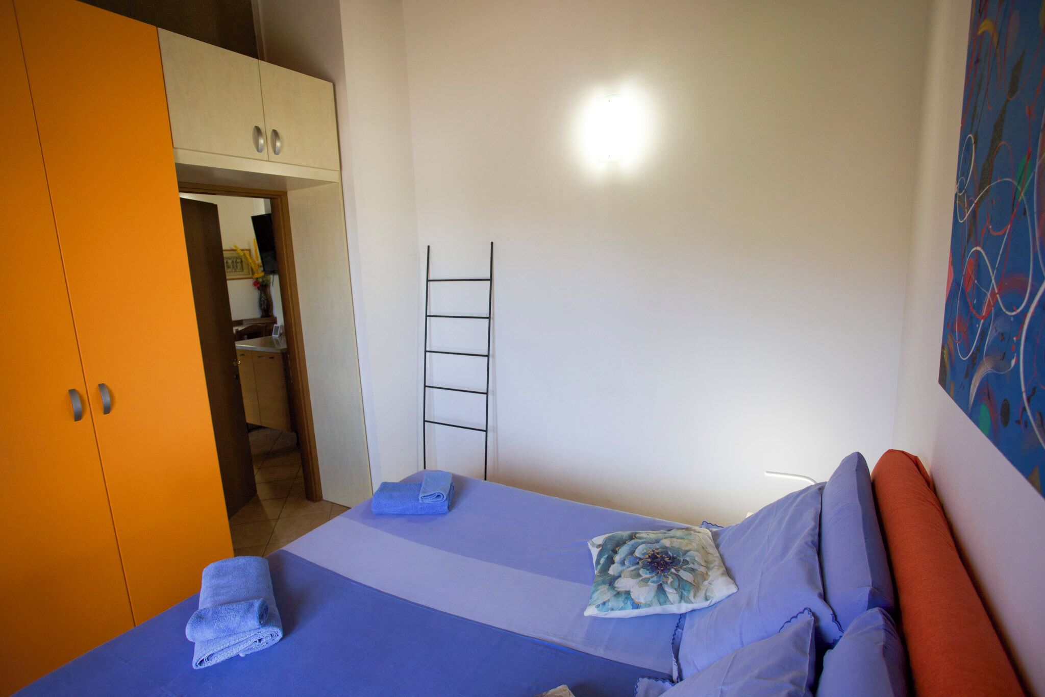 A bedroom with a bed, a wardrobe, a ladder, and a painting on the wall.