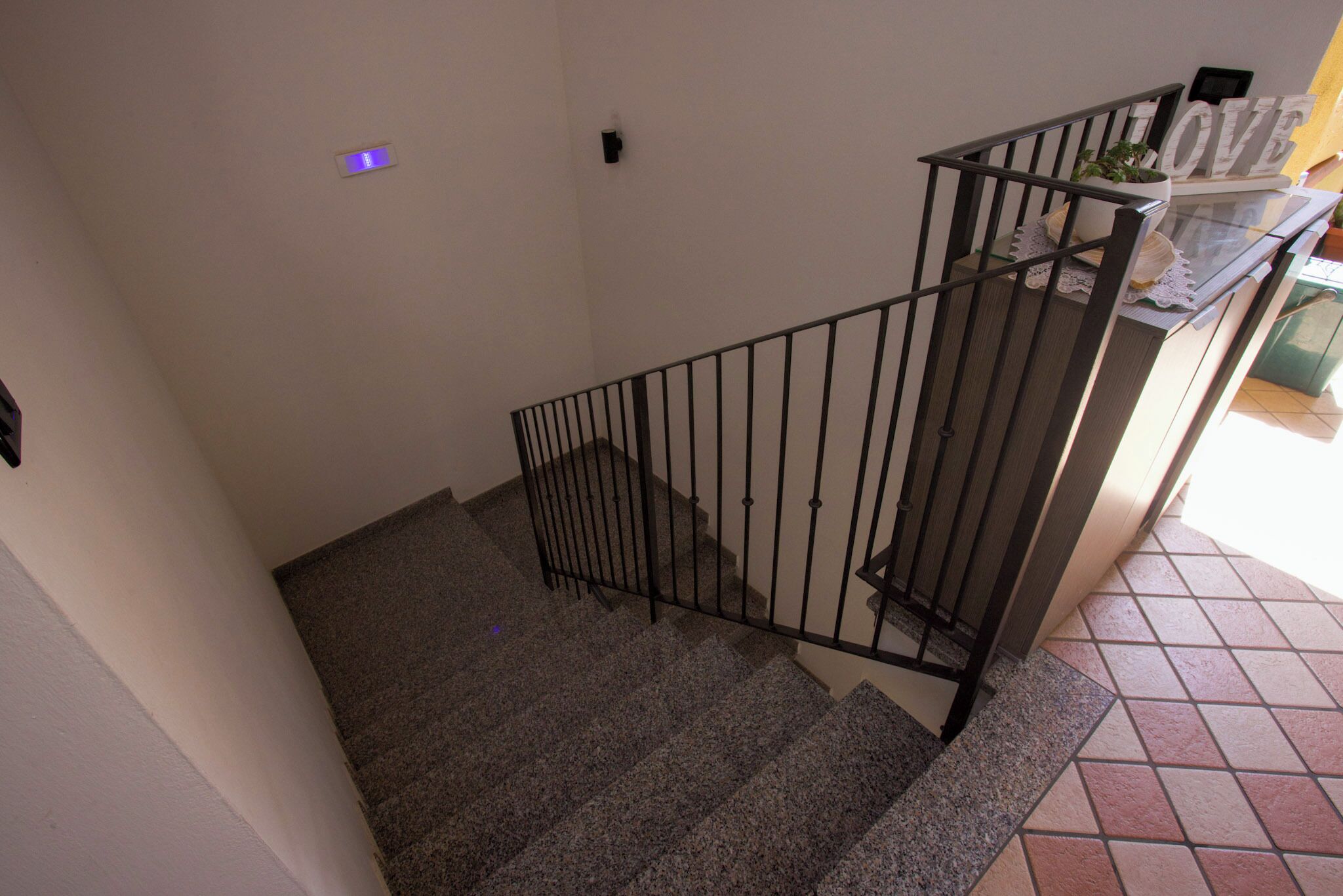 A staircase with a metal railing, a potted plant on the landing, and a tiled floor.