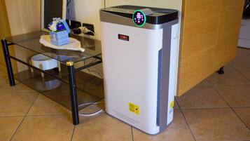A white air purifier with a digital display on top, placed on a tiled floor next to a glass table with a decorative item.