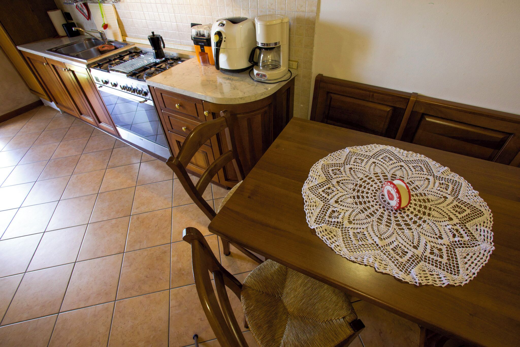 Una cocina con estufa, cafetera y una mesa con un mantel de encaje.