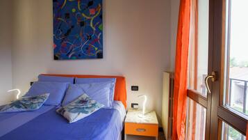 Un dormitorio con cama, mesita de noche, lámpara, un cuadro en la pared y ventana con cortinas.