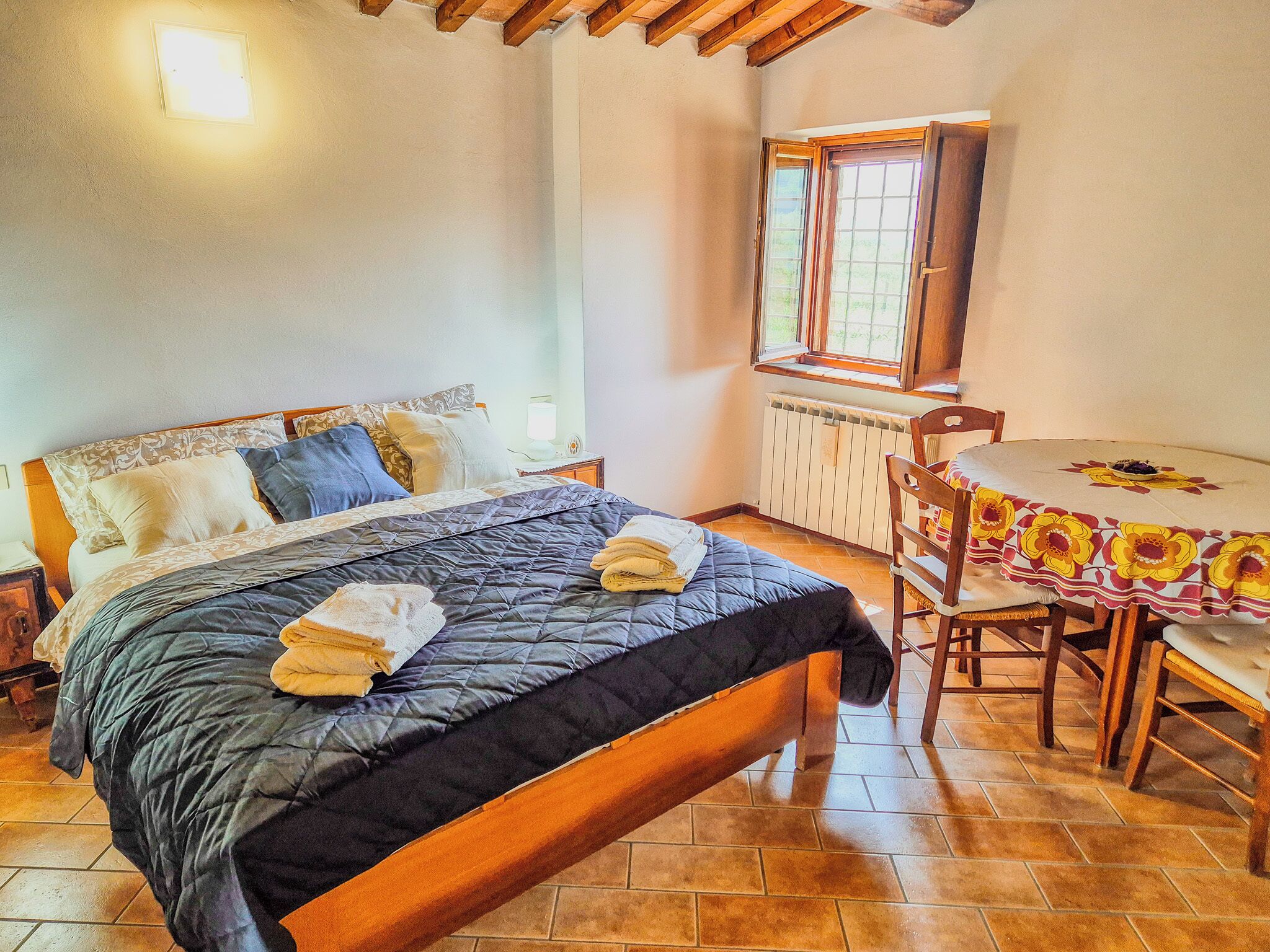 A bedroom with a bed, a table, chairs, a window, and a radiator.