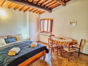 Een slaapkamer met een bed, een klein rond tafeltje met stoelen, een raam en een radiator.