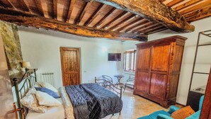 A bedroom with a bed, a wooden wardrobe, a small table with chairs, and a window.