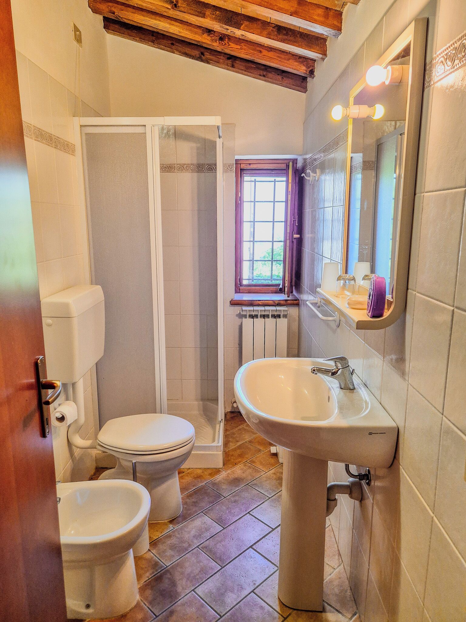 Un bagno con toilette, bidet, doccia, lavandino e una finestra con vista.