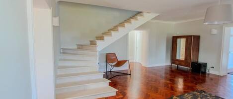 Ein geräumiges Zimmer mit Holzboden, einer Treppe, einem braunen Ledersessel und einem gemusterten Teppich.