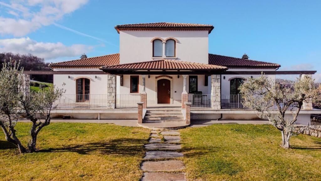 A two-story house with a tiled roof, a stone facade, and a front entrance with steps leading up to it.