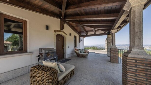 A covered patio with stone flooring, a grill, wicker furniture, and a view of the landscape. - Affittacamere Profumo Campestre (Frigento)