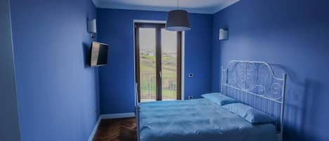 A bedroom with a bed, a television, and a door leading to a balcony.