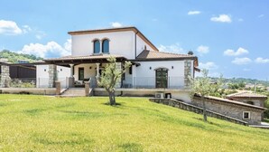 A two-story house with a white facade, a tiled roof, and a stone foundation. There is a small garden in front with a tree and a stone wall. - Affittacamere Profumo Campestre (Frigento)