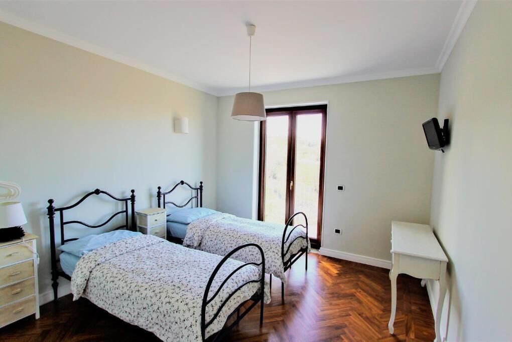 A bedroom with two beds, a desk, and a TV on the wall.