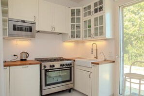 A kitchen with white cabinets, a stainless steel stove, a built-in oven, and a window to the right.