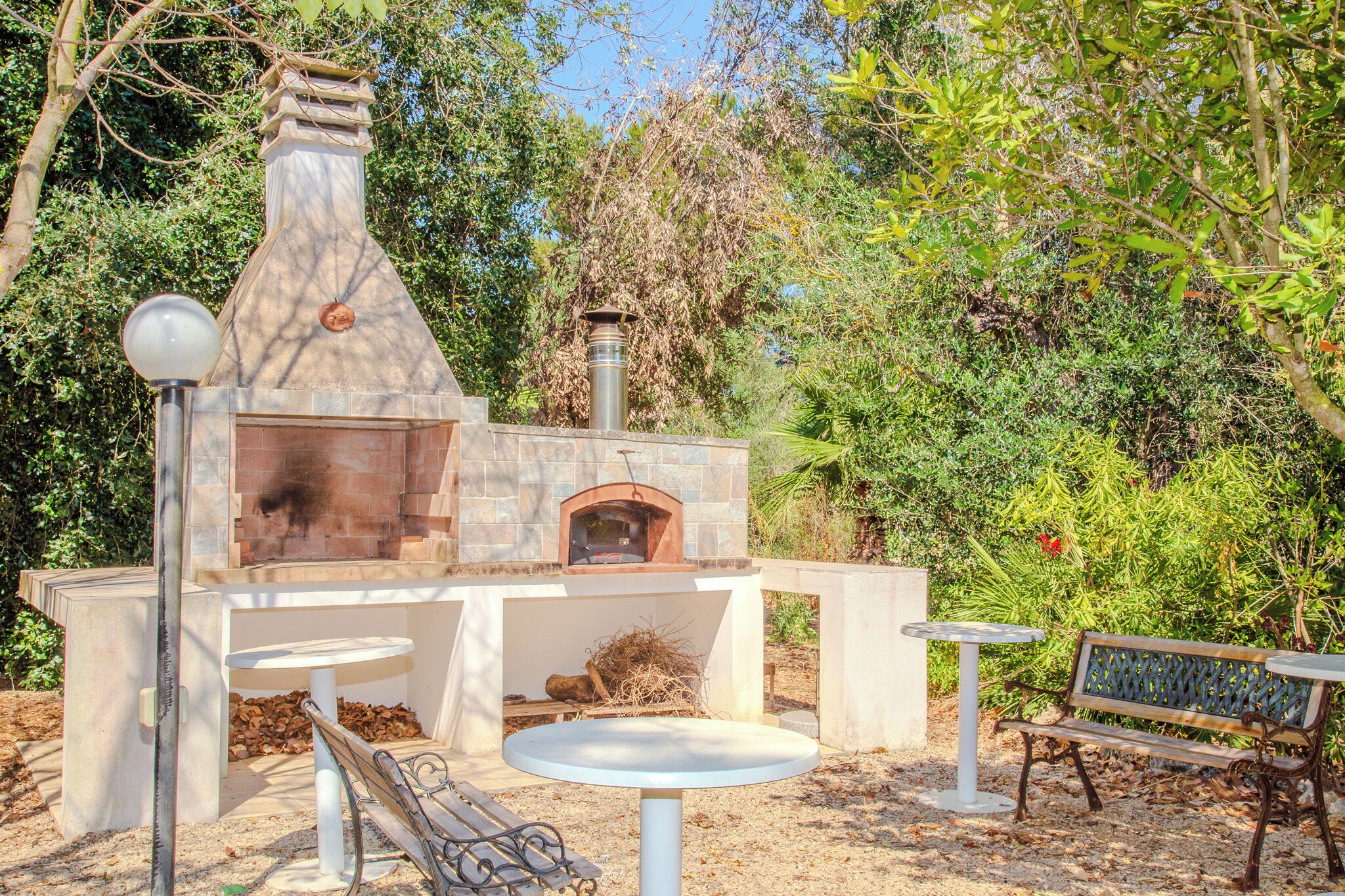 An outdoor brick oven with a chimney, surrounded by greenery and a bench.