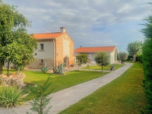 A two-story house with a red-tiled roof, surrounded by a well-maintained lawn and various plants. - Villa Nides (Monselice)