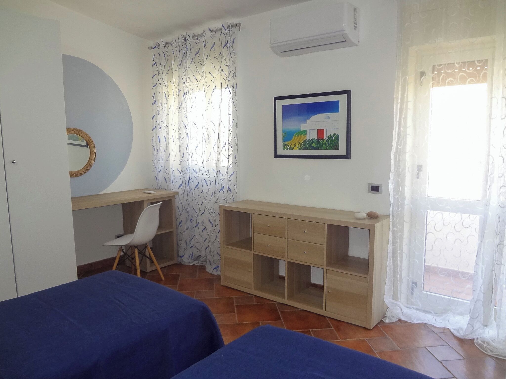 A room with two beds, a desk, a chair, a wardrobe, and a window with curtains.