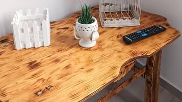 Une table en bois au design rustique, une petite clôture décorative blanche, une petite plante en pot, une cage à oiseaux blanche et une télécommande.