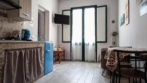 A compact kitchen with a blue refrigerator, a dining table with chairs, and a patterned rug. - Casa Al Porticciolo (Trapani)