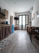 A compact kitchen with a blue refrigerator, a dining table with chairs, and a patterned rug.