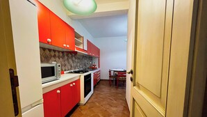 A compact kitchen with red cabinets, a microwave, a stove, and a dining table with chairs. - Casa Vacanza Acquanuova (Calatafimi)
