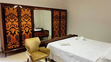 A hotel room with a large bed, a chair, a wardrobe with ornate designs, and a mirror.