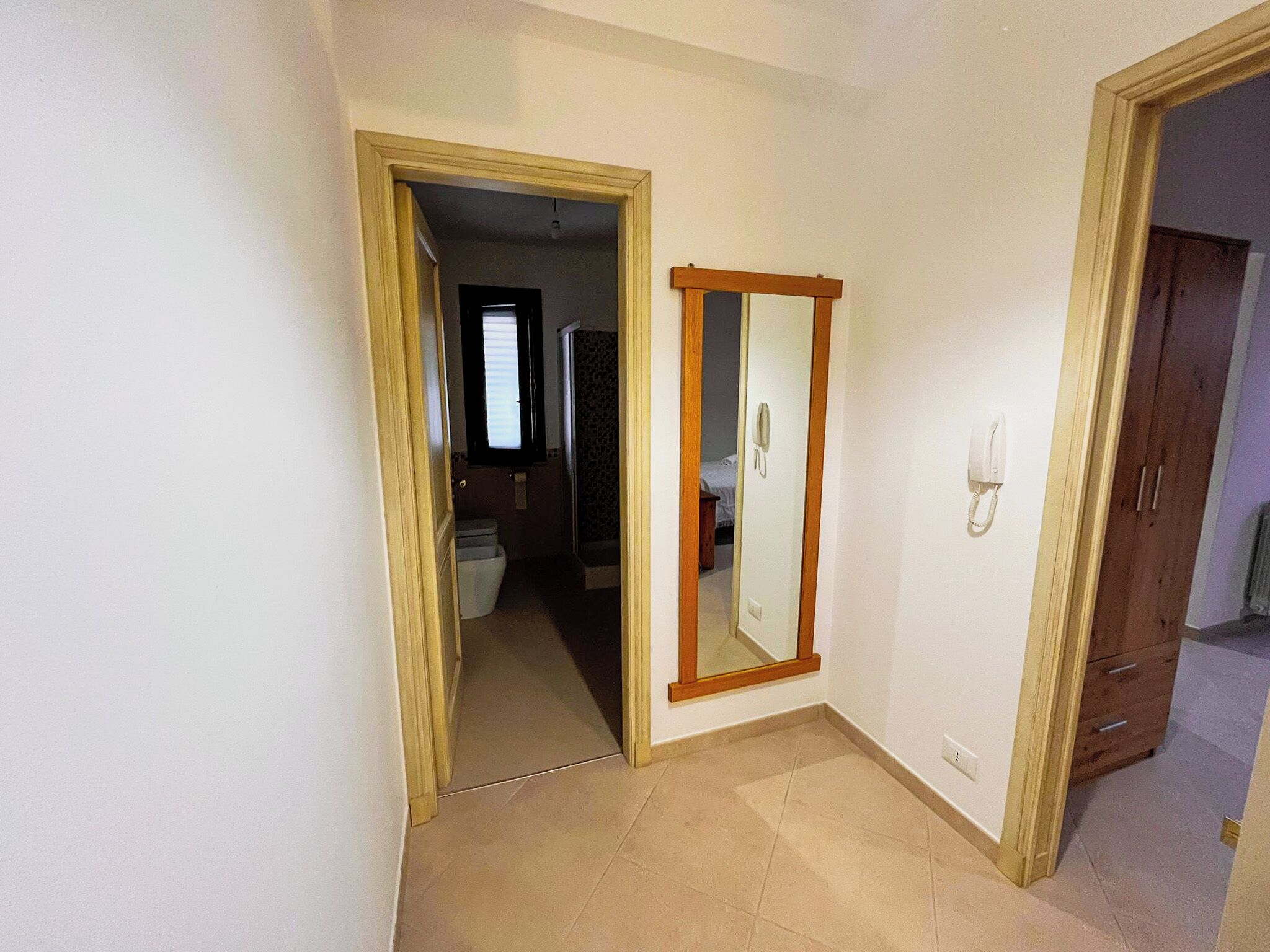 A room with a wooden door, a mirror, and a telephone on the wall.