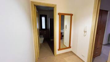 A room with a wooden door, a mirror, and a telephone on the wall.